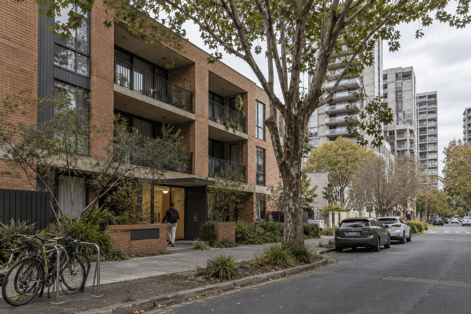 A modest low-rise apartment block and taller residential buildings along a tree-lined street.