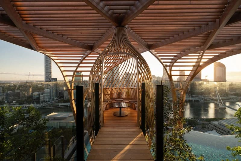 Timber ribs frame a rooftop walkway and a woven pod at Upper House, with Brisbane beyond.